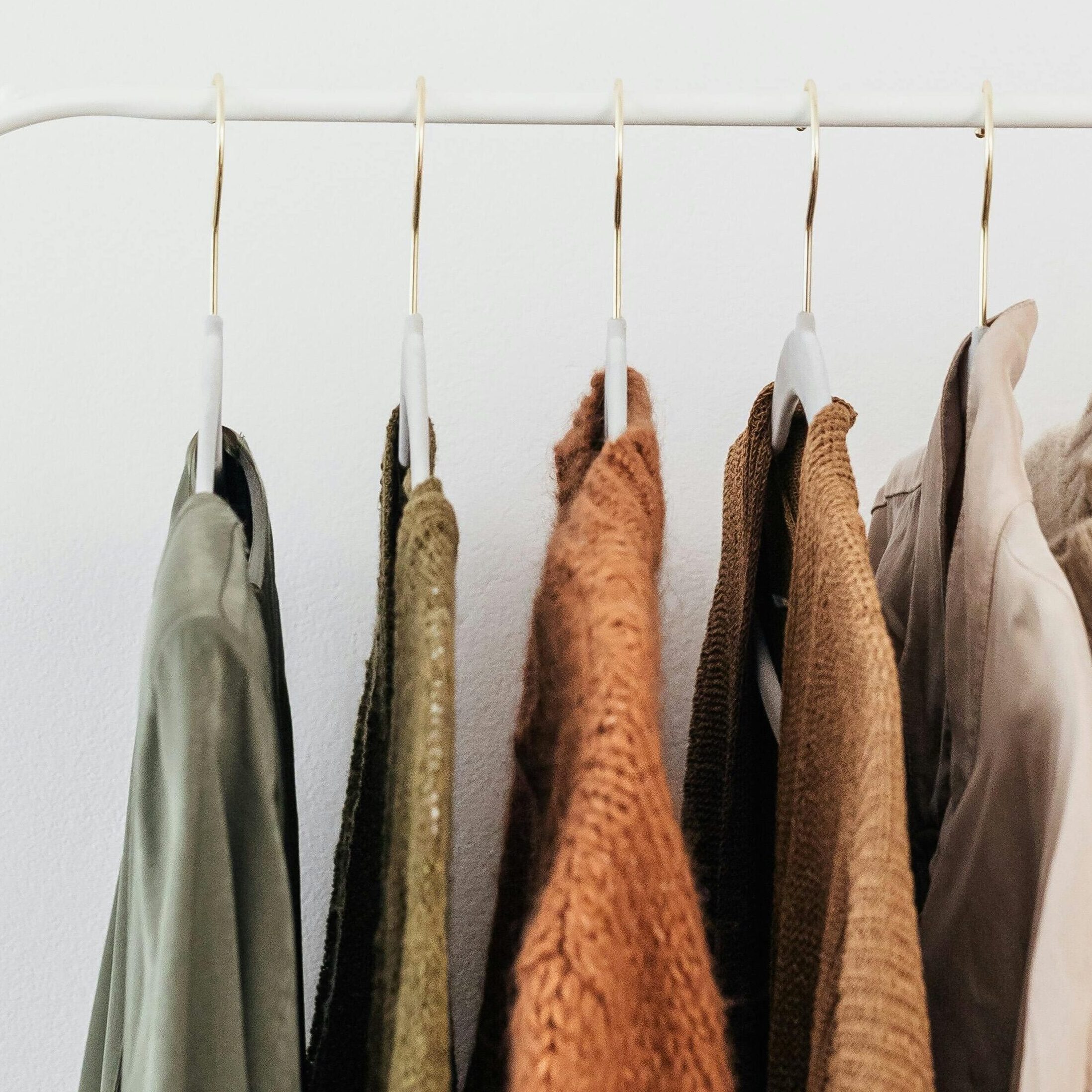 Elegant neutral-toned clothes hanging on a white rail against a plain background, perfect for fashion themes.