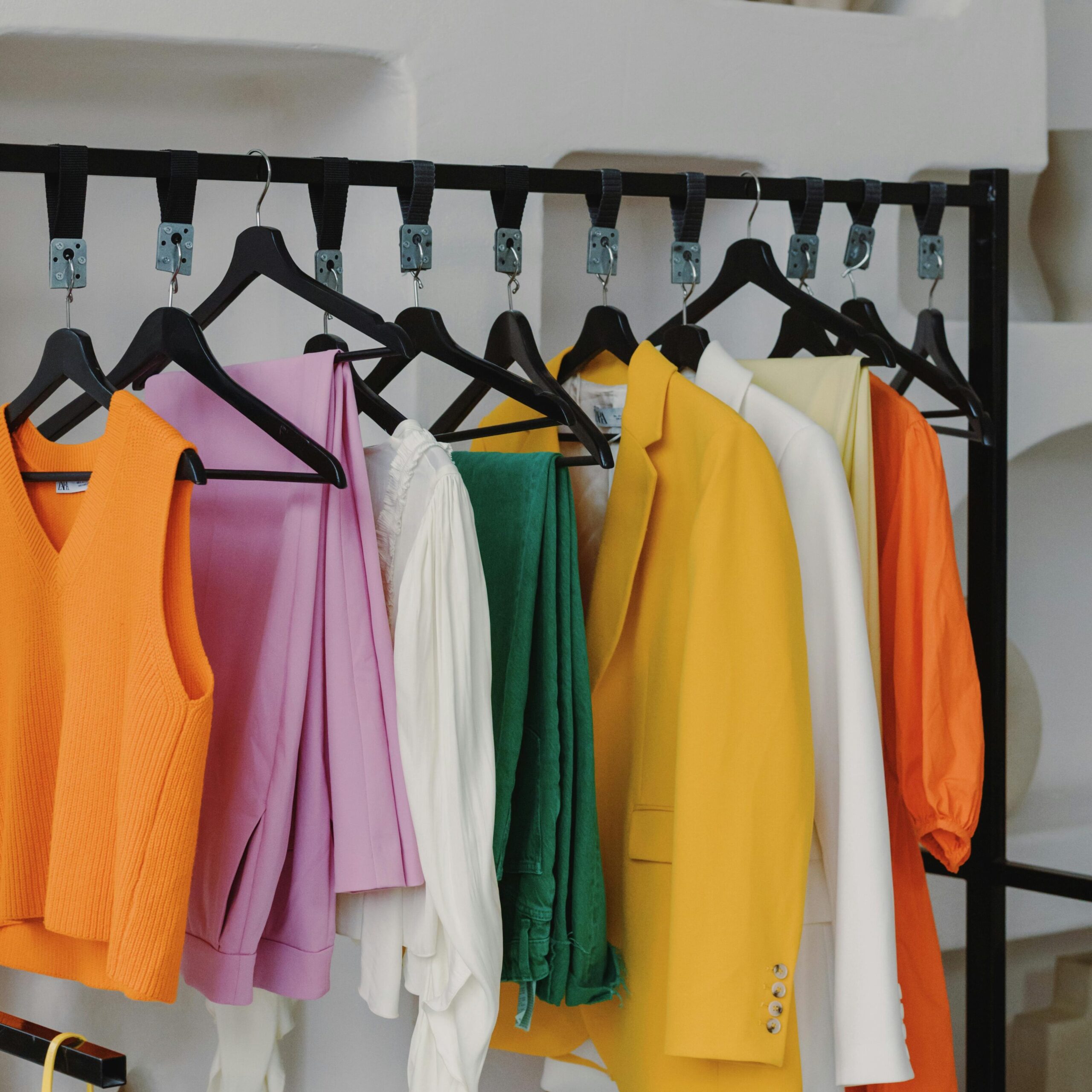 Vibrant assortment of clothes elegantly displayed on a modern clothing rack against an artistic white backdrop.